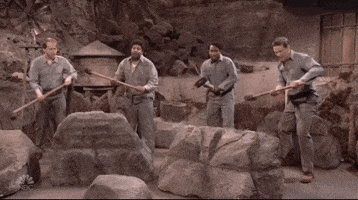 Four men swinging pickaxes at a pile of rocks